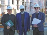 three men in suit jackets stand in white hard hats