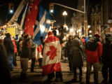 Crowd of protesters at night, waving Canadian and other flags. Participants wear winter clothing, creating a lively, determined atmosphere with glowing streetlights.