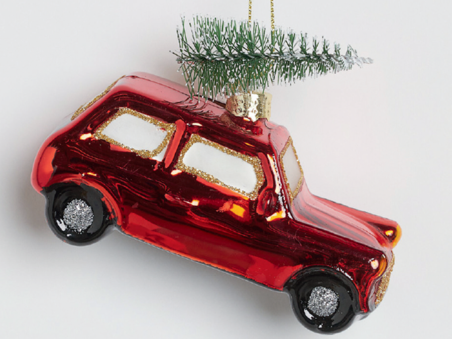 A red, glossy car-shaped ornament with a small green Christmas tree on top. The car has gold accents and black wheels, creating a festive tone.