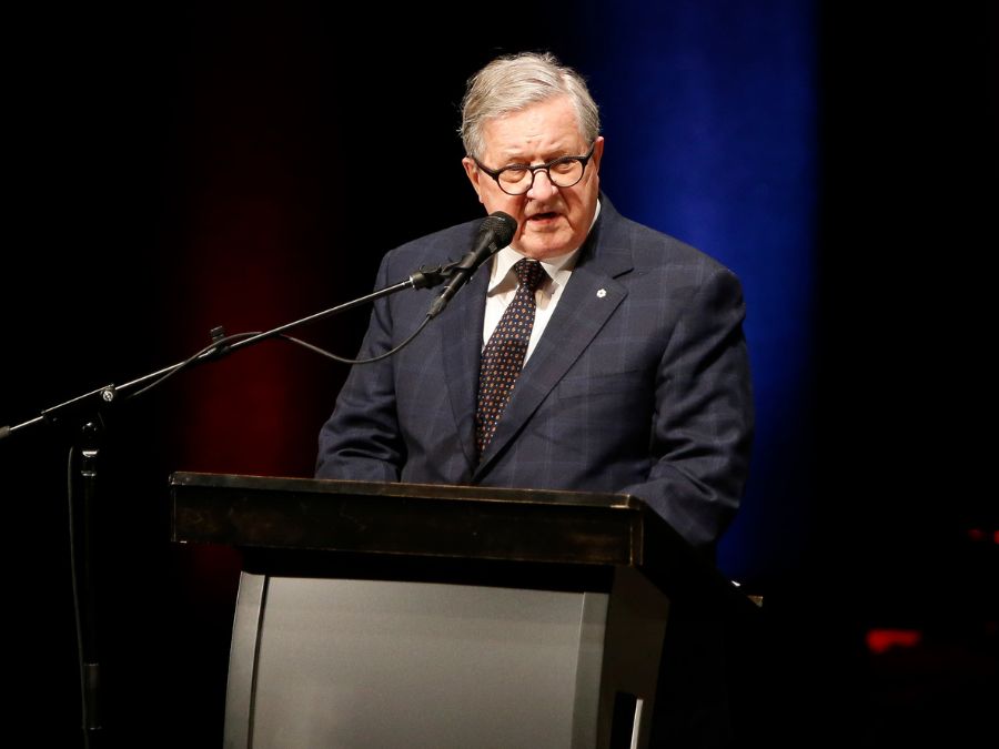 A Caucasian man in glasses and a suit talks at a podium