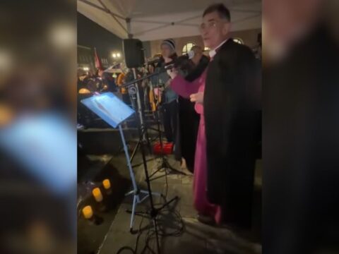 A man in clerical robes stands on a stage at an event