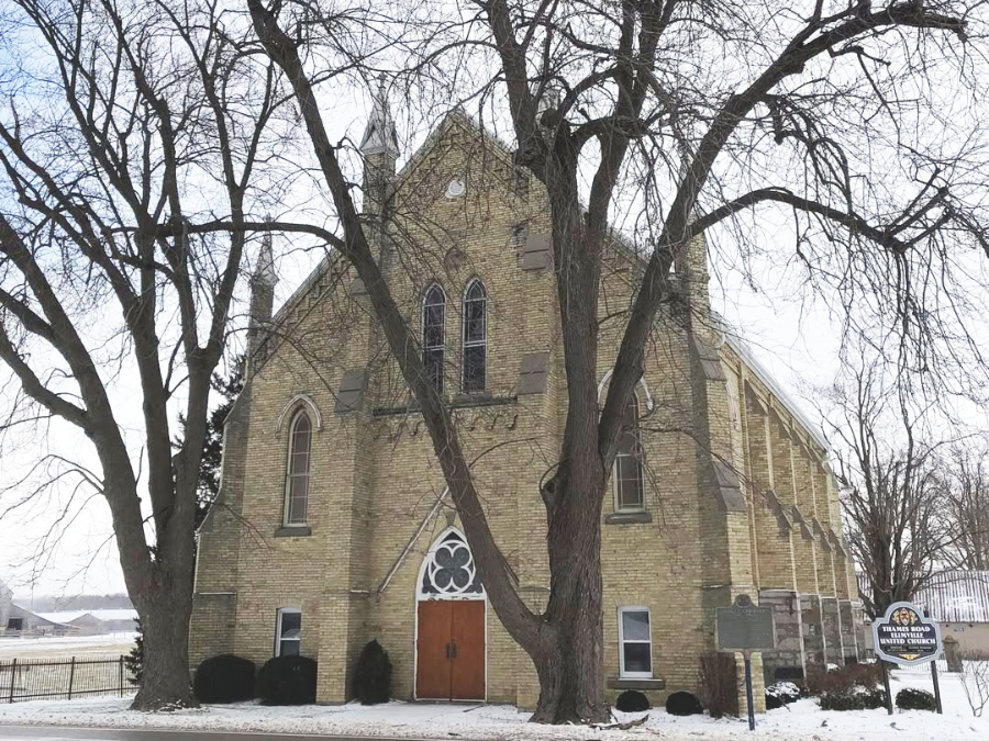 Historic stone church on a snowy day, featuring tall arched windows, a wooden door, and bare winter trees framing the entrance. Peaceful atmosphere.