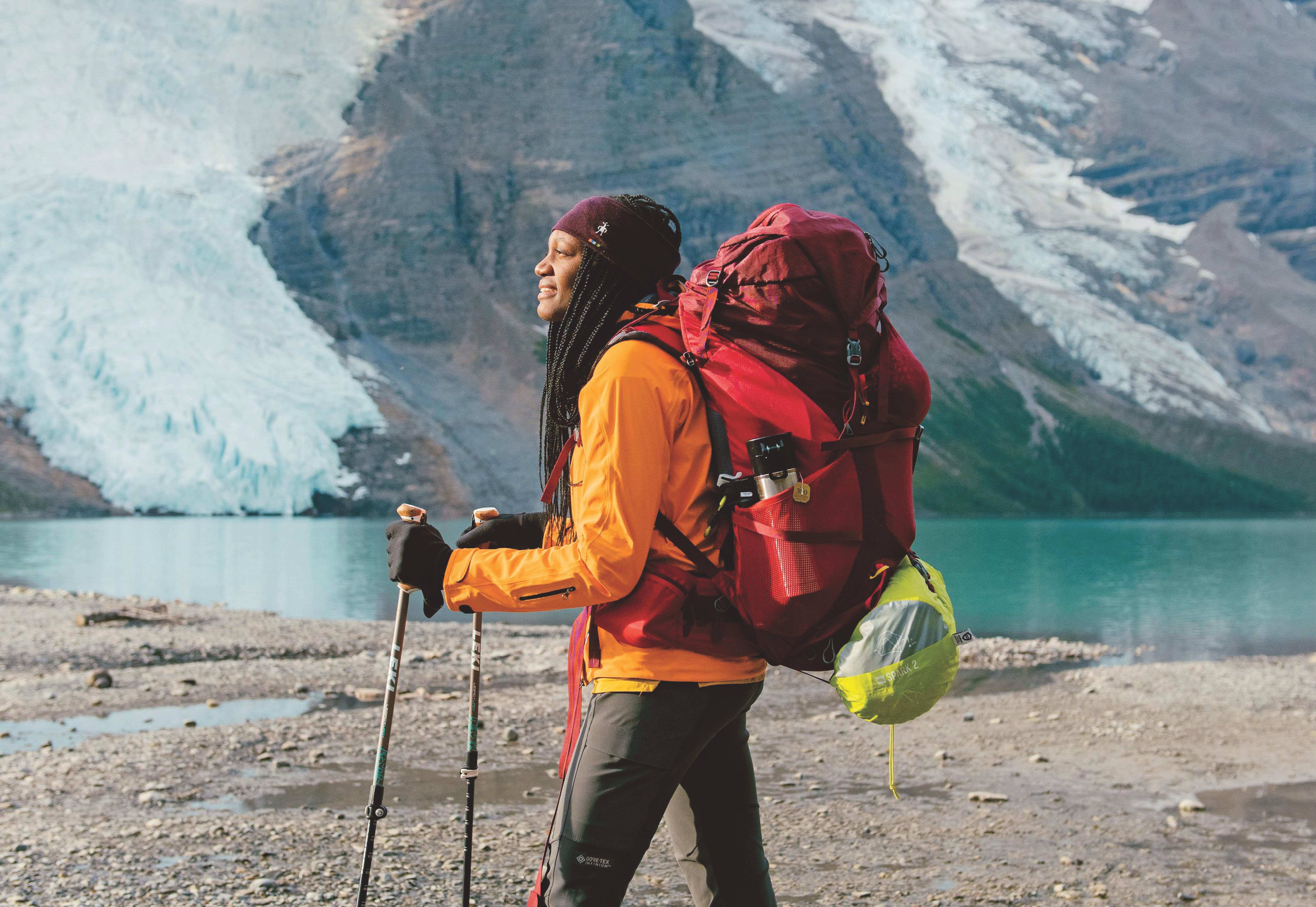 A person in hiking gear with a red backpack walks by a serene lake and glaciers. The setting is mountainous, conveying an adventurous and uplifting tone.