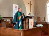 a Caucasian man in ministers' garb stands at pulpit in a church