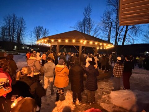 People stand holding candles near a gazebo